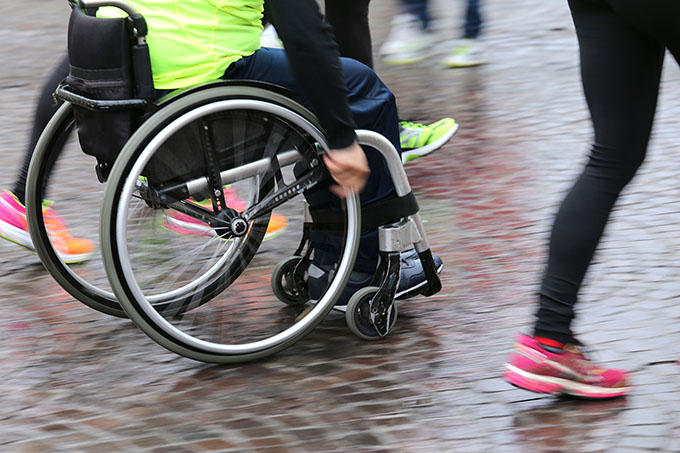 Persona en silla de ruedas mostrando movimiento junto a personas corriendo.