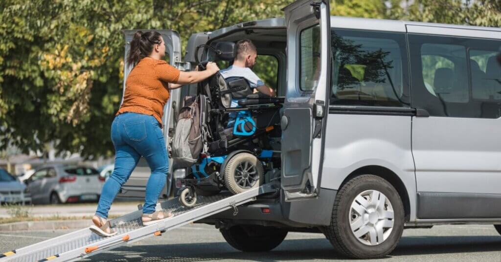 A woman pushes a man in a wheelchair up a ramp into a van in a parking lot, showcasing the convenience of rear-entry wheelchair accessible vehicles.