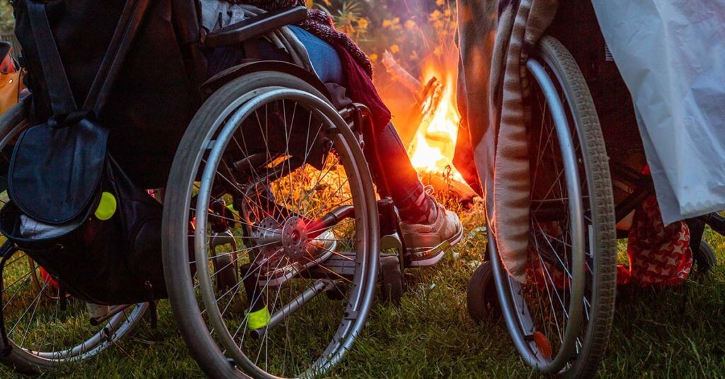 Dos personas en sillas de ruedas disfrutando de una fogata en la noche de verano. Vista a las ruedas de las sillas de ruedas durante la noche en la chimenea