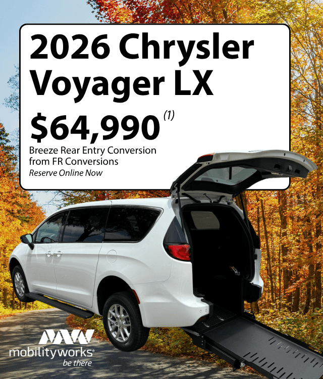 White 2026 Chrysler Voyager LX with a rear entry wheelchair ramp extended, parked on a road with autumn trees. Check out MobilityWorks promotions above for price and conversion details.