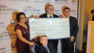 Four adults present a $30,000 donation check for GAN research to a young man in a wheelchair during an All in for Ethan fundraising event, held in honor of Rare Disease Day.