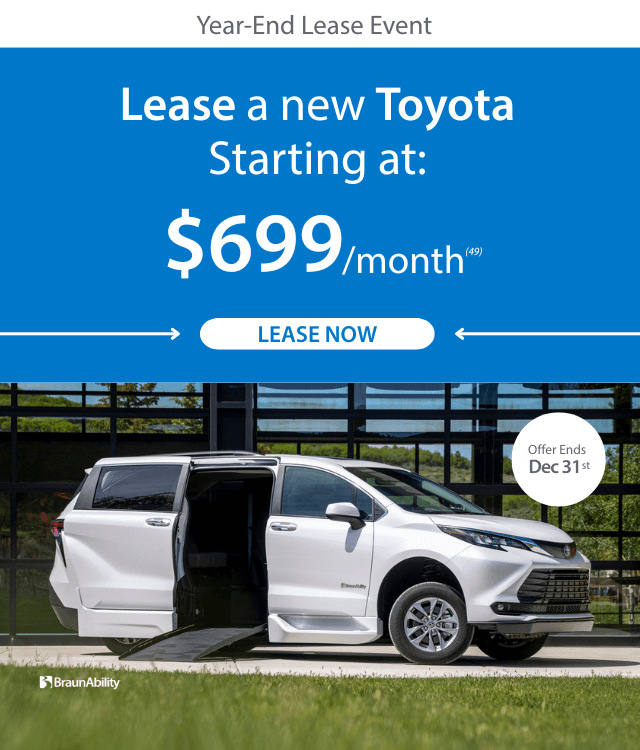 White Toyota minivan with a wheelchair ramp extended, parked in front of a glass building. Banner advertises lease offer at $699/month, ending December 31.
