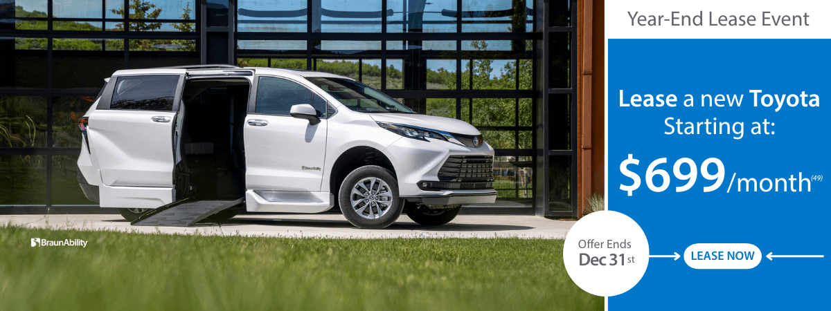 A white Toyota minivan with an open sliding door is parked in front of a building; a banner advertises a year-end lease event starting at $699/month.