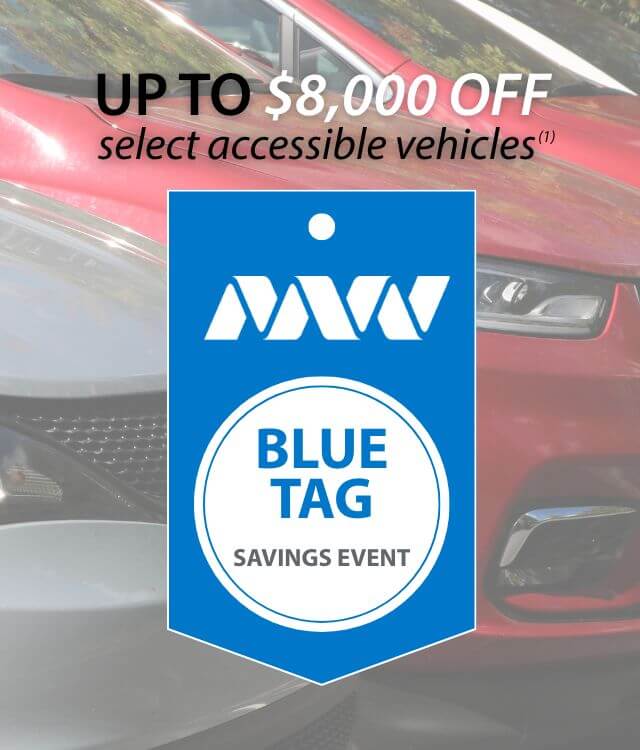 Blue tag savings event promotion sign offering up to $8,000 off select accessible vehicles, with a close-up of a red car in the background.