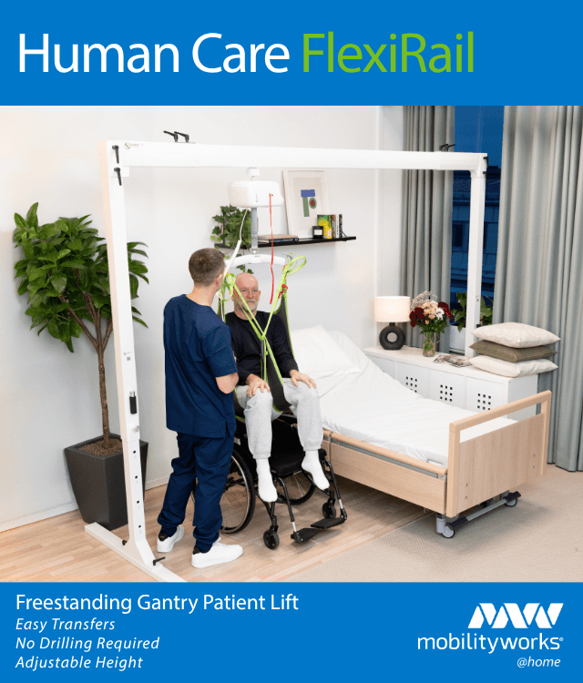 A healthcare worker operates a patient lift, transferring an older man from a wheelchair to a bed in a modern, accessible bedroom.