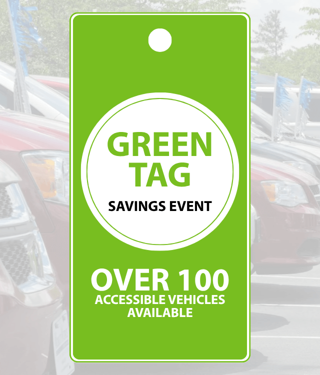 Green tag sign reads “Green Tag Savings Event. Over 100 accessible vehicles available” in front of a row of parked cars.