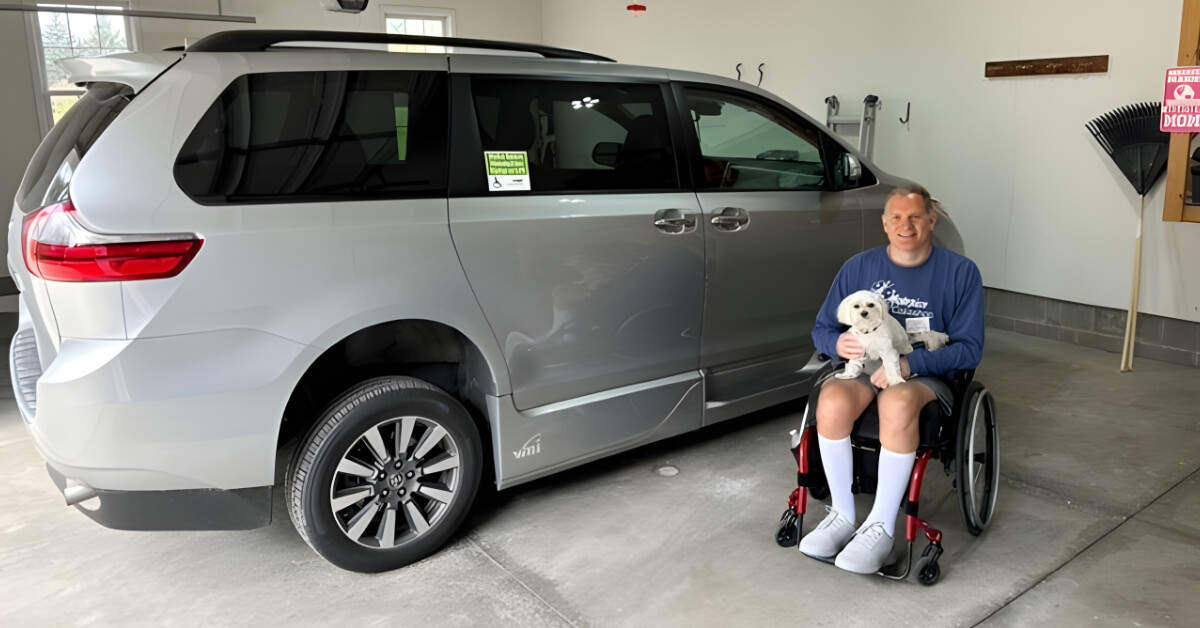 Dr. Jason Kolb poses next to his new accessible van with his small white dog on his lap.