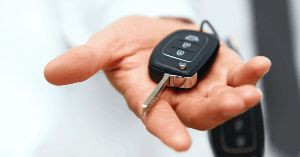 A person extends their hand holding a modern car key with a remote control fob toward the camera, highlighting the convenience of wheelchair van leasing.
