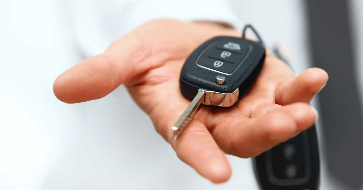 A person extends their hand holding a modern car key with a remote control fob toward the camera, highlighting the convenience of wheelchair van leasing.