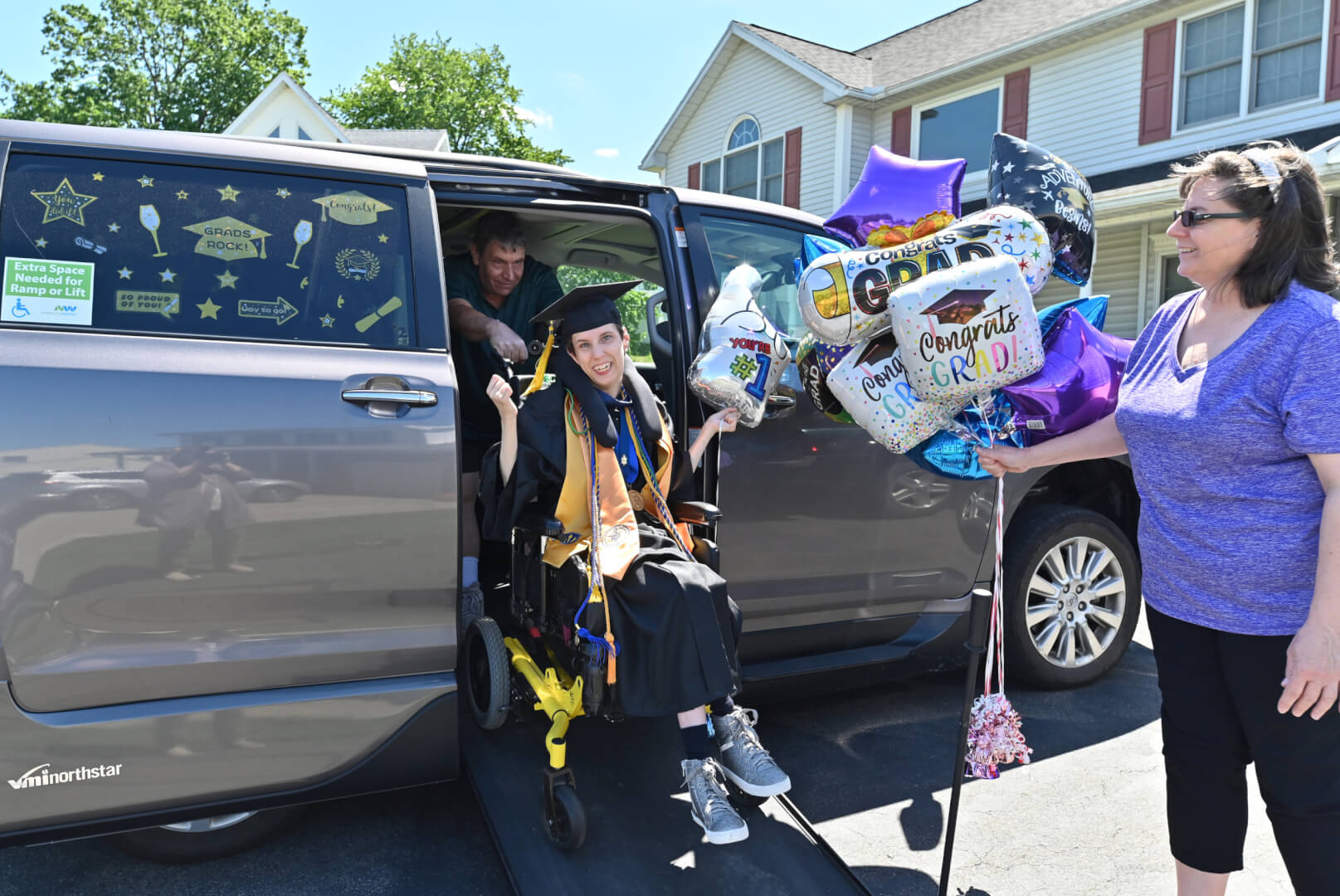 Lizzie and her family are all smiles on graduation day as she exits her accessible van in her cap and gown.