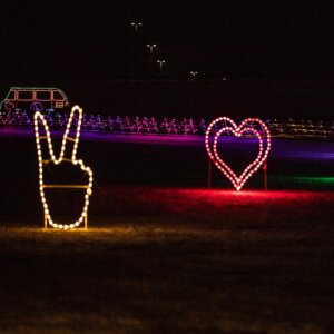 Luces navideñas con forma de mano dando el signo de la paz y un corazón hecho de luces.