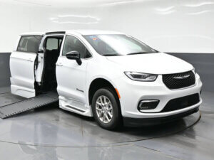 White minivan with both side doors open and a wheelchair ramp extended from the passenger side on a glossy showroom floor, showcasing the latest MobilityWorks promotions.