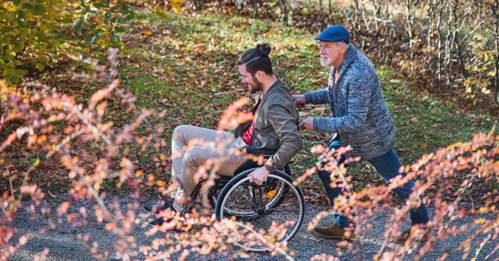 Padre mayor y su hijo en silla de ruedas a pie en la naturaleza.