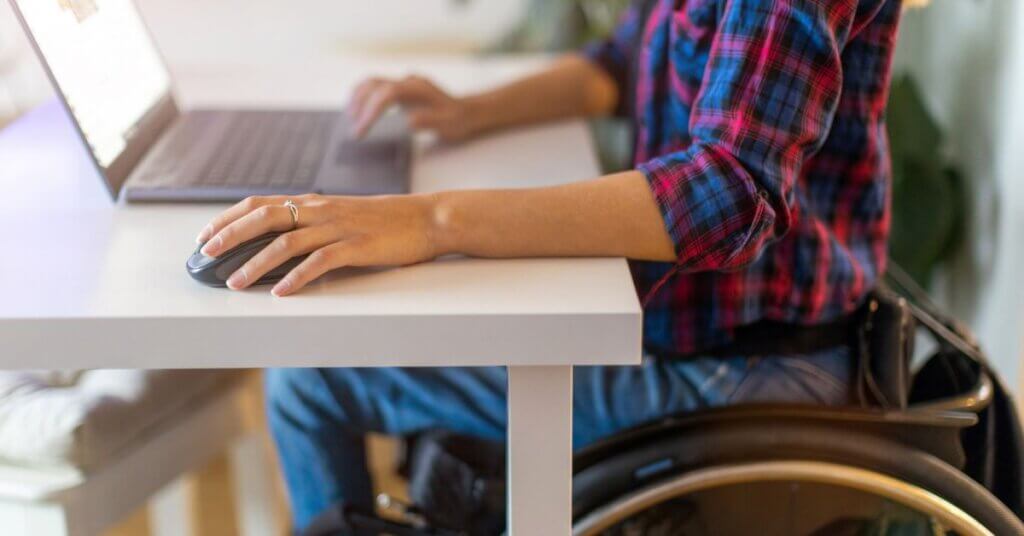 Woman in wheelchair using laptop in office