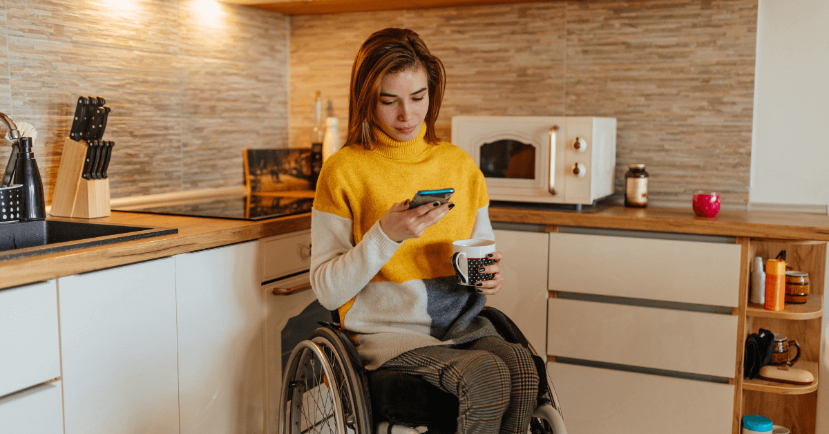 Mujer en silla de ruedas tomando café y usando el teléfono en casa