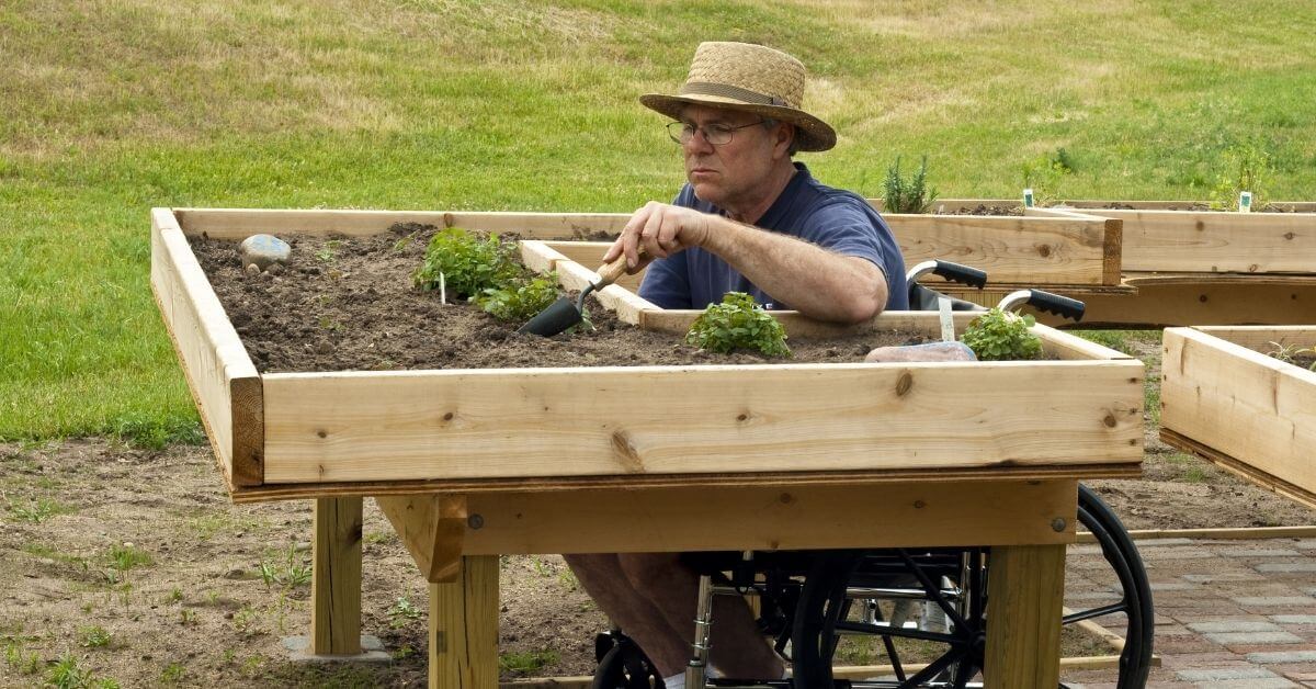 Hombre en silla de ruedas trabajando en una mesa de jardín habilitadora