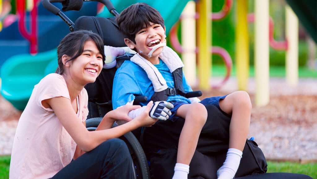 Boy in wheelchair sitting with sister on grass