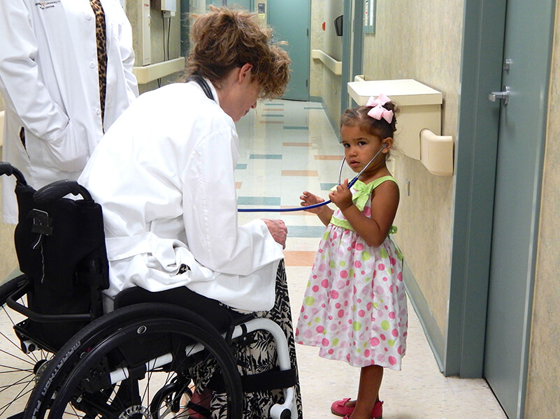 doctor in wheelchair lets young girl use stethoscope
