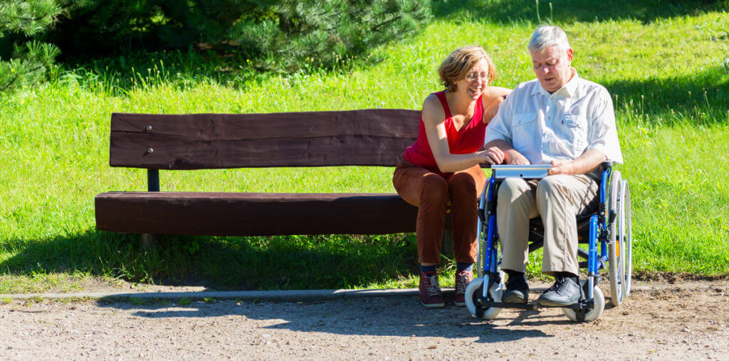 Man in a wheelchair with his wife in the park looking at a tablet

