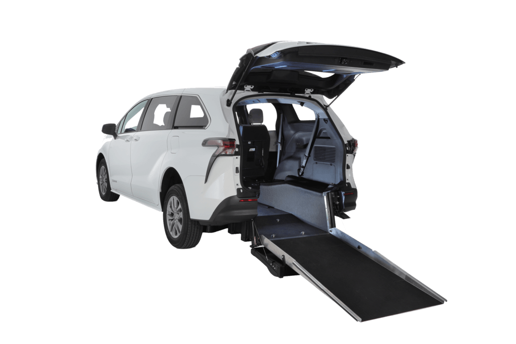 A white minivan with its rear hatch open and a wheelchair-accessible ramp extended from the back, showing the spacious interior.
