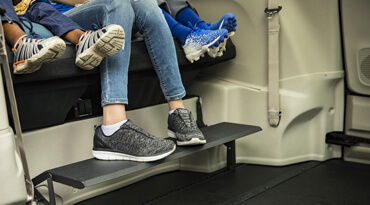 The feet and legs of a women and two kids on a foot rest in a wheelchair van 