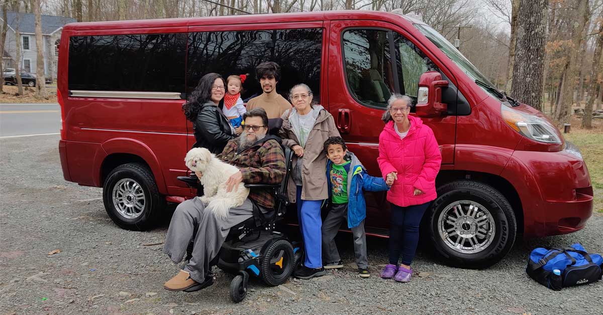 Familia de pie delante de la furgoneta roja para sillas de ruedas