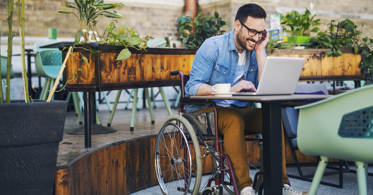 Hombre en silla de ruedas en el café al aire libre en una computadora