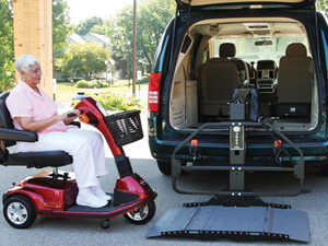 Anciana conduciendo scooter rojo en el elevador de la silla de ruedas en la parte trasera de la minivan