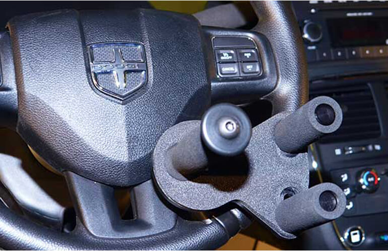 A black driving aid device attached to the black steering wheel of a Dodge vehicle