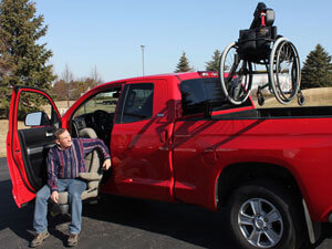 Red pickup truck with hoist lift in bed of truck and person sitting on a turning seat