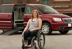 Mujeres en silla de ruedas frente a una camioneta Chrystler roja accesible para sillas de ruedas con la puerta de entrada lateral abierta