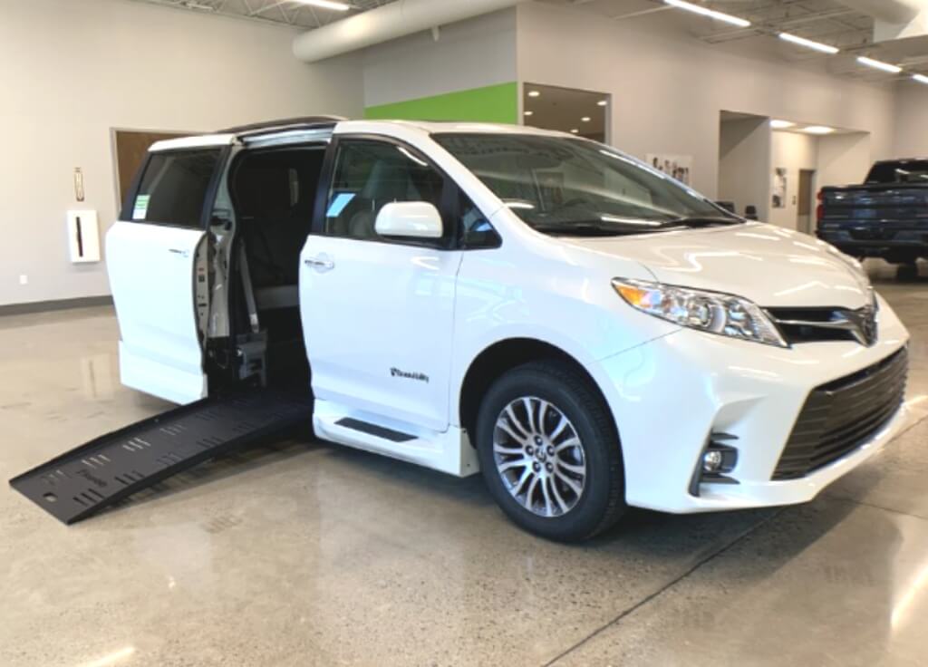 Una furgoneta para silla de ruedas Toyota Sienna blanca con la rampa de entrada lateral desplegada