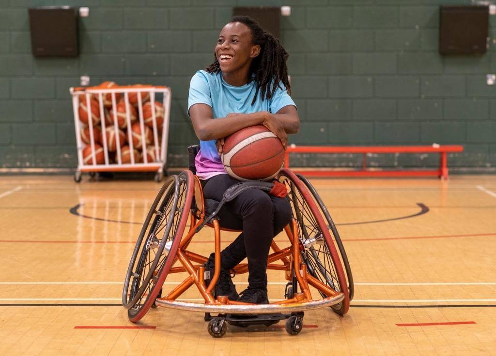 Chica sentada en una silla de ruedas sosteniendo una pelota de baloncesto en una cancha de baloncesto